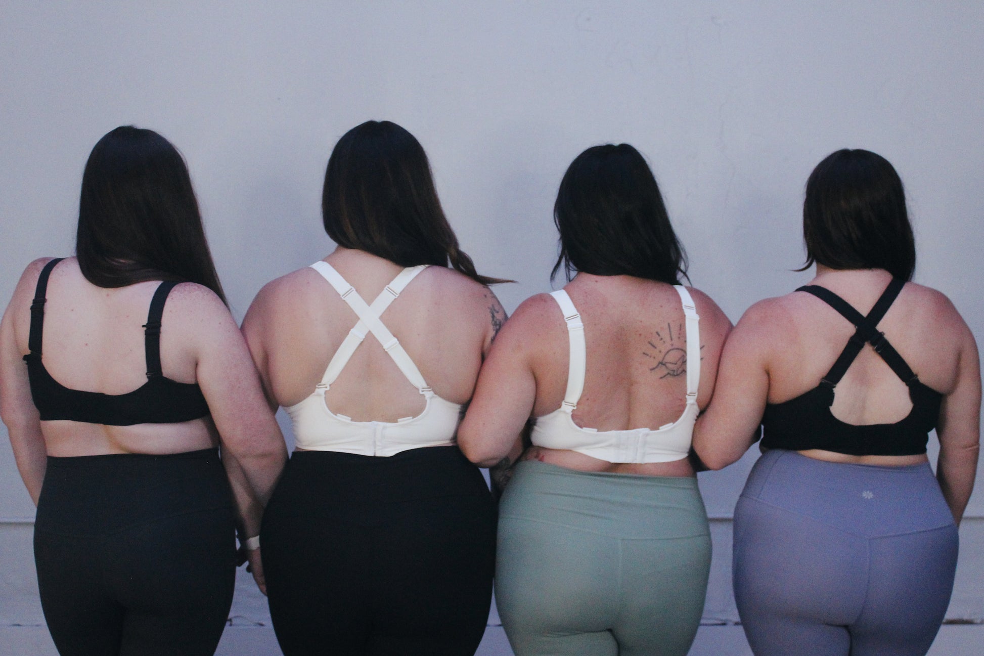 Four women wearing medium to high support bras for short torsos but full cups, in a range of sizes H cup to G cup.